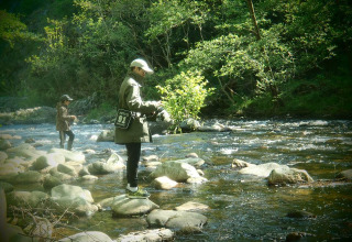 Two people fishing in a rocky river surrounded by forest at Ushuaïa Villages Le Viaduc campsite in France.