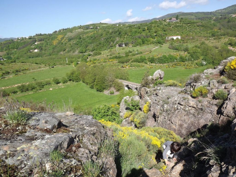 A child climbs rocky terrain with lush green fields and hills at Ushuaïa Villages Le Viaduc campsite, France.