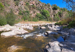 Photo of a rocky stream and lush hillside under a blue sky at Ushuaïa Villages Le Viaduc campsite in France.