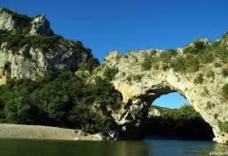 Natural stone arch above a river near Arlebosc, Auvergne-Rhône-Alpes, France, surrounded by lush greenery.