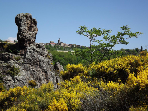 Scenic view of large rocks, yellow flowers, and a distant village in Auvergne-Rhône-Alpes, France.
