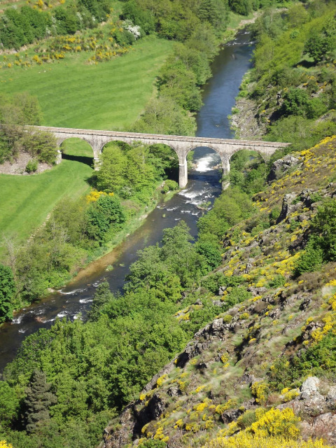 Viadotto di pietra sopra un fiume circondato da campi verdi e colline vicino al campeggio Ushuaïa Villages Le Viaduc in Francia.