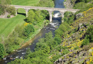 Viadotto di pietra sopra un fiume circondato da campi verdi e colline vicino al campeggio Ushuaïa Villages Le Viaduc in Francia.