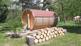 Barrel-shaped wooden pod with a stack of logs in front at Ushuaïa Villages Le Viaduc Campsite, France.