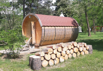 Træhytte formet som en tønde med træstammebunke foran, ved Ushuaïa Villages Le Viaduc Camping, Frankrig.
