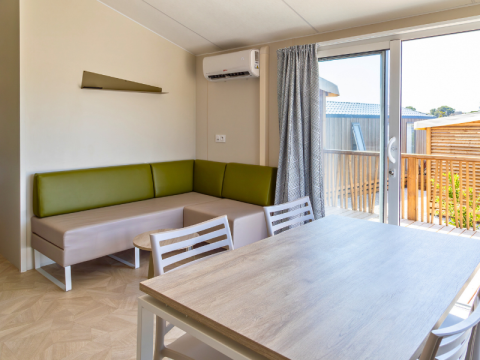 Soggiorno di chalet moderno con divano verde, tavolo da pranzo e accesso alla terrazza al Camping Les Tamaris, Francia.