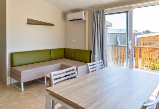 Soggiorno di chalet moderno con divano verde, tavolo da pranzo e accesso alla terrazza al Camping Les Tamaris, Francia.