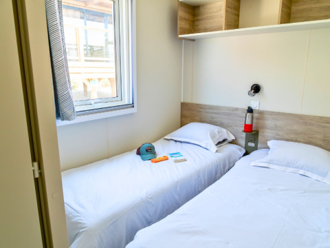 Camera con due letti singoli, finestra, mensole e oggetti personali nel Premium Mobile Home a Les Tamaris.