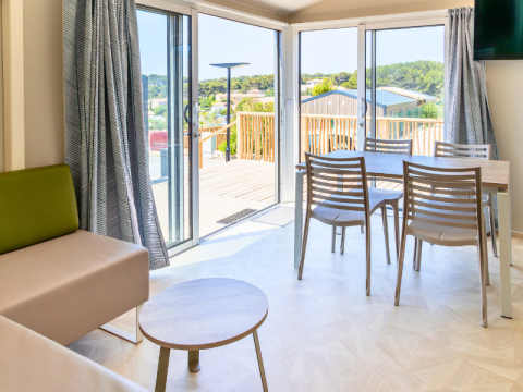 Interno luminoso di una casa mobile premium con zona pranzo e terrazza al campeggio Les Tamaris, Francia.