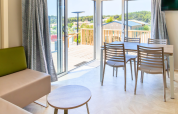 Interno luminoso di una casa mobile premium con zona pranzo e terrazza al campeggio Les Tamaris, Francia.