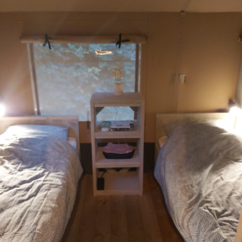 Dos camas individuales en una tienda safari Ranger Lodge en Petite Suisse, Bélgica, separadas por un estante.