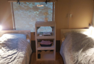 Dos camas individuales en una tienda safari Ranger Lodge en Petite Suisse, Bélgica, separadas por un estante.