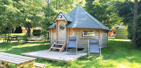 Finnish kota wooden lodge with two deck chairs outside, surrounded by green trees at Campsite Ushuaïa Villages Le Viaduc.
