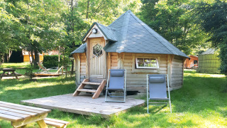 Finnische Kota-Holzhütte mit zwei Liegestühlen davor inmitten von Natur im Ushuaïa Villages Le Viaduc Campingplatz.