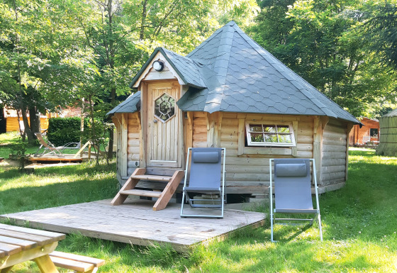 Cabane en bois de style kota finlandais avec deux transats devant, entourée d’arbres au camping Ushuaïa Villages Le Viaduc.