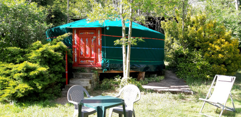 Una yurta verde con puerta roja decorada, rodeada de plantas y muebles de jardín en Ushuaïa Villages Le Viaduc.