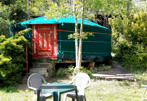 A green yurt with a decorated red door, surrounded by greenery and garden furniture at Ushuaïa Villages Le Viaduc.