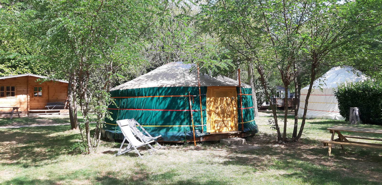 Yurt tent op Campsite Ushuaïa Villages Le Viaduc in Frankrijk, omgeven door bomen en picknickbanken.