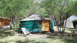Tienda yurta en el camping Ushuaïa Villages Le Viaduc en Francia, rodeada de árboles y bancos.