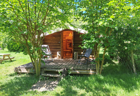 Træhytte med terrasse og stole, omgivet af grønne træer på Campsite Ushuaïa Villages Le Viaduc, Frankrig.