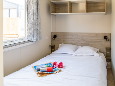 Soveværelse med dobbelt seng og åbent vindue i Premium Mobile Home på Camping Les Tamaris, Frankrig.
