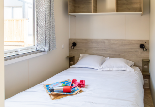 Soveværelse med dobbelt seng og åbent vindue i Premium Mobile Home på Camping Les Tamaris, Frankrig.