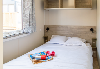 Soveværelse med dobbelt seng og åbent vindue i Premium Mobile Home på Camping Les Tamaris, Frankrig.