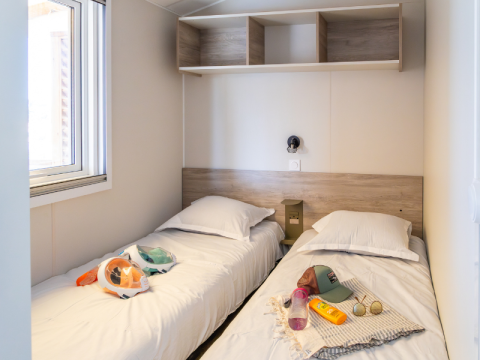 To enkeltsenge i et lyst værelse med vindue, sengetøj og strandtilbehør i Premium Mobile Home, Les Tamaris.