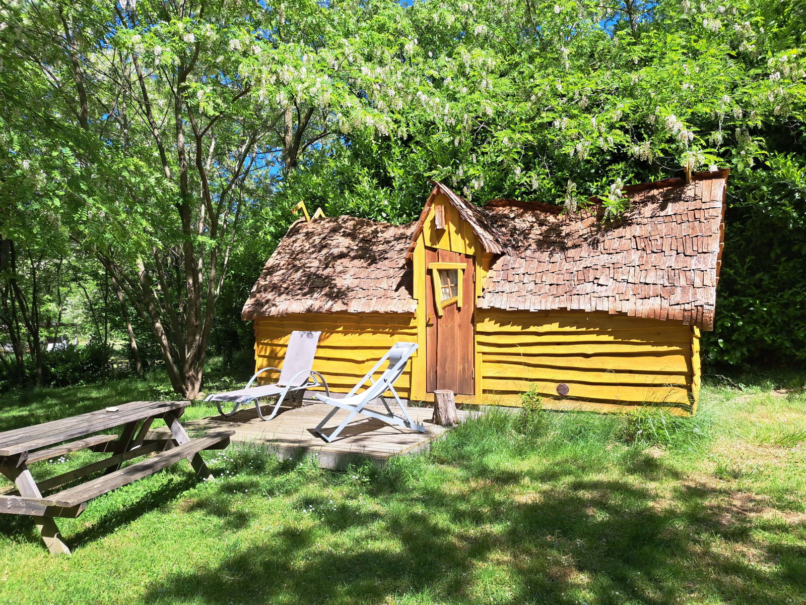 Gele blokhut genaamd Magic hut op Camping Ushuaïa Villages Le Viaduc in Frankrijk, omgeven door bomen.