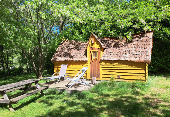 Gul træhytte kaldet Magic hut på Campsite Ushuaïa Villages Le Viaduc i Frankrig, omgivet af træer.