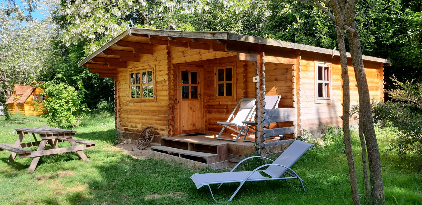 Houten blokhut bij Ranch Chalet, omgeven door bomen, met ligstoelen, ligbed en picknicktafel buiten.
