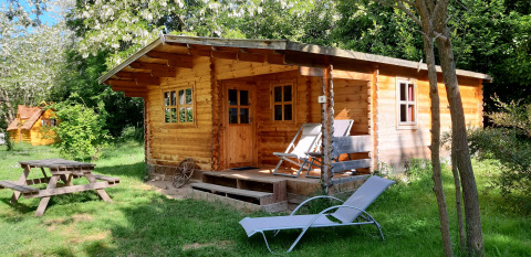 Chalet in legno al Ranch Chalet immerso nel verde, con sedie a sdraio, lettino e tavolo da picnic.