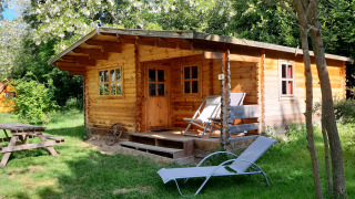Wooden cabin at Ranch Chalet surrounded by trees, featuring deck chairs, a lounge chair, and picnic table.