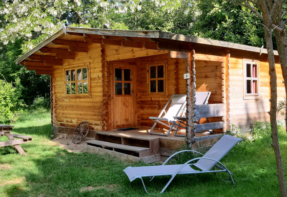 Chalet in legno al Ranch Chalet immerso nel verde, con sedie a sdraio, lettino e tavolo da picnic.