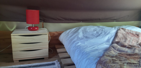 Safari tent interieur met houten ladekast, rode lamp en palletbed in Bivouac Tent, Le Viaduc, Frankrijk.