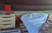 Safari tent interieur met houten kastje, rode lamp en palletbed in Bivouac Tent, Le Viaduc, Frankrijk.