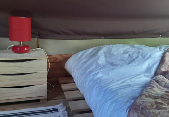 Interno tenda safari con cassettiera in legno, lampada rossa e letto a pallet nella Bivouac Tent, Le Viaduc, Francia.