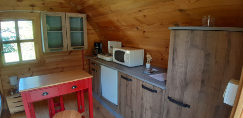Accogliente angolo cucina in legno in un pod al campeggio Ushuaïa Villages Le Viaduc con tavolo rosso e microonde.
