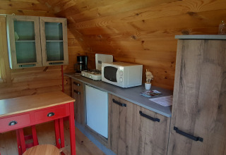 Accogliente angolo cucina in legno in un pod al campeggio Ushuaïa Villages Le Viaduc con tavolo rosso e microonde.