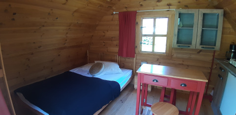 Interno di una pod in legno con letto, tavolo e armadietto al campeggio Ushuaïa Villages Le Viaduc, Francia.