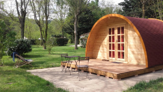 Pod in legno con terrazza e mobili da giardino al campeggio Ushuaïa Villages Le Viaduc in Francia, tra gli alberi.