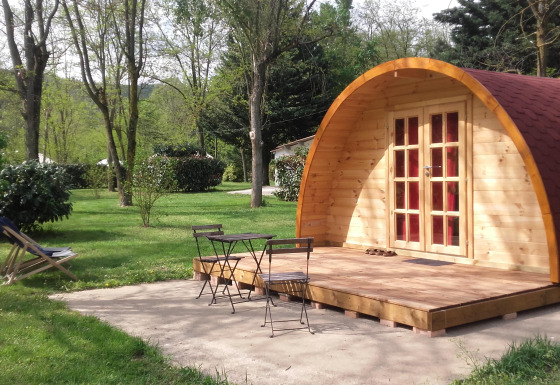 Pod in legno con terrazza e mobili da giardino al campeggio Ushuaïa Villages Le Viaduc in Francia, tra gli alberi.