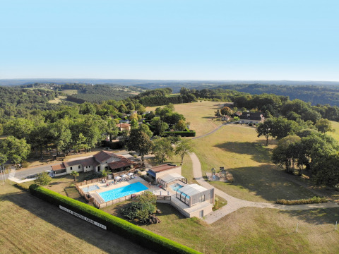 Aerial view of La Nouvelle Croze campsite featuring a pool, vacation homes, and forested landscape in France.