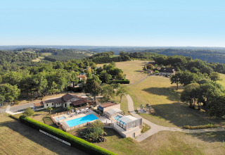 Aerial view of La Nouvelle Croze campsite featuring a pool, vacation homes, and forested landscape in France.