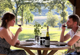 A couple enjoys wine at an outdoor table with scenic views at Campsite La Nouvelle Croze in France.