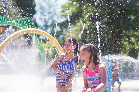 Due bambini sorridenti giocano nelle fontane d'acqua al campeggio La Nouvelle Croze, Nouvelle-Aquitaine, Francia.