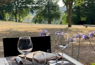 Tavolo apparecchiato all'aperto con bicchieri da vino, menù e vista panoramica presso un campeggio in Francia.
