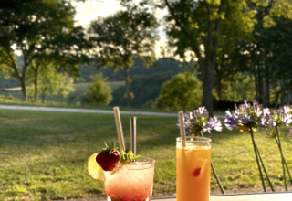 Due cocktail freschi su un tavolo al tramonto con vista sulla natura al campeggio La Nouvelle Croze, Francia.
