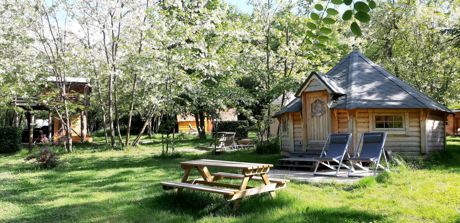 Finse kota blokhut met ligstoelen en picknicktafel op de groene camping Ushuaïa Villages Le Viaduc.