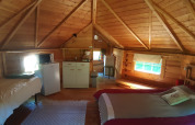 Innenraum einer Holzhütte im finnischen Kota-Stil mit zwei Betten, Küchenzeile, Fenster und rustikalem Charme.